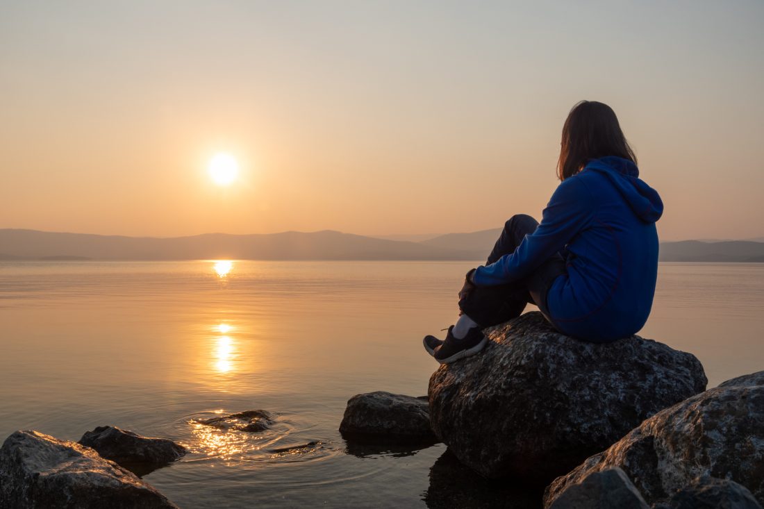 Tiener vrouw kijkt naar zee/water - zonsondergang