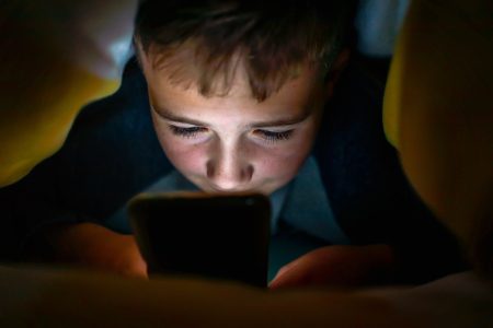 Jong kind onder de deken met smartphone